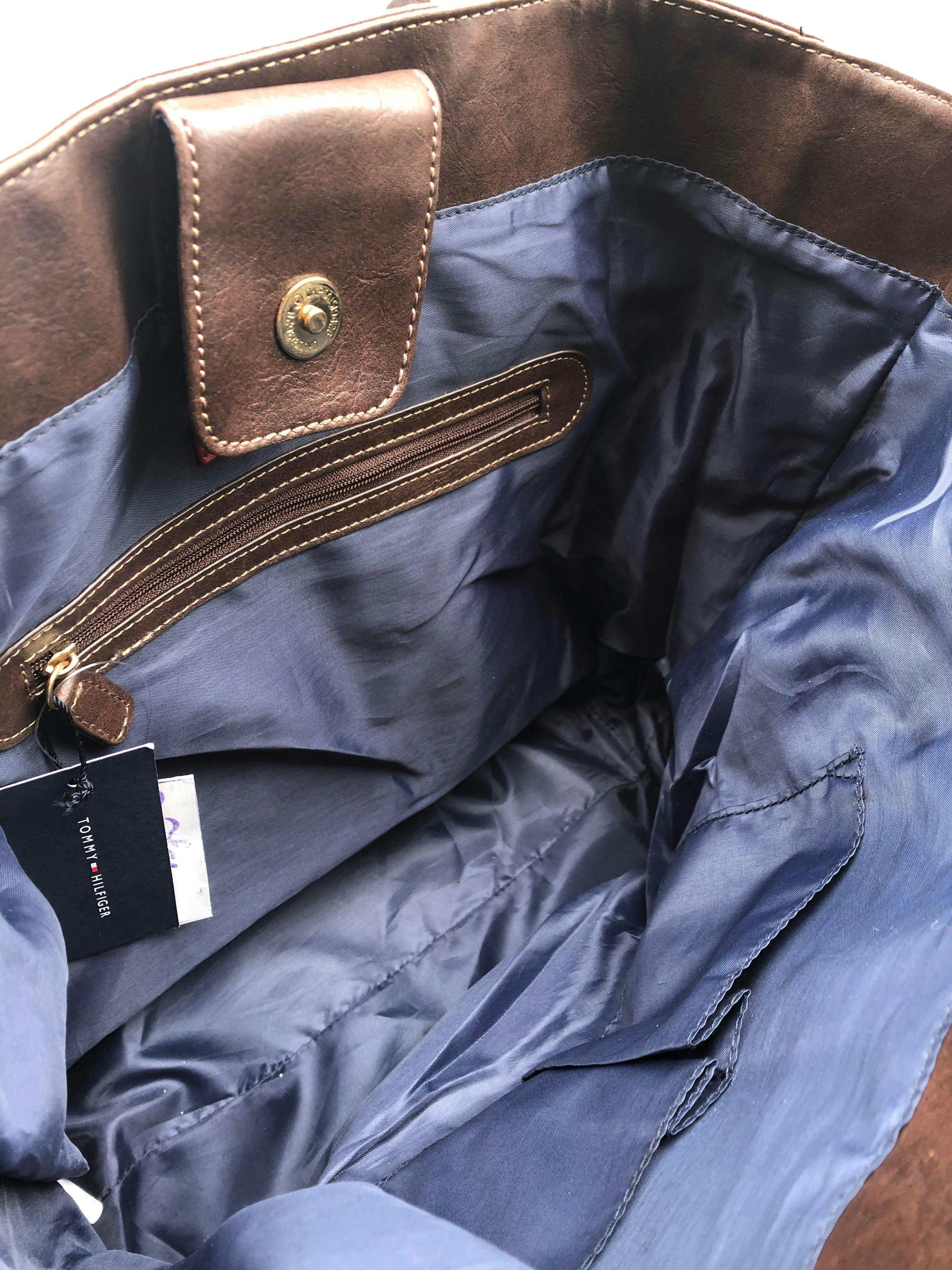 Cartera Tommy Hilfiger monograma azul y rojo con detalles tipo cuero marrón, forro interno con un compartimento con zipper, cierra co broche. Medidas 34x33x12cm.  Nueva