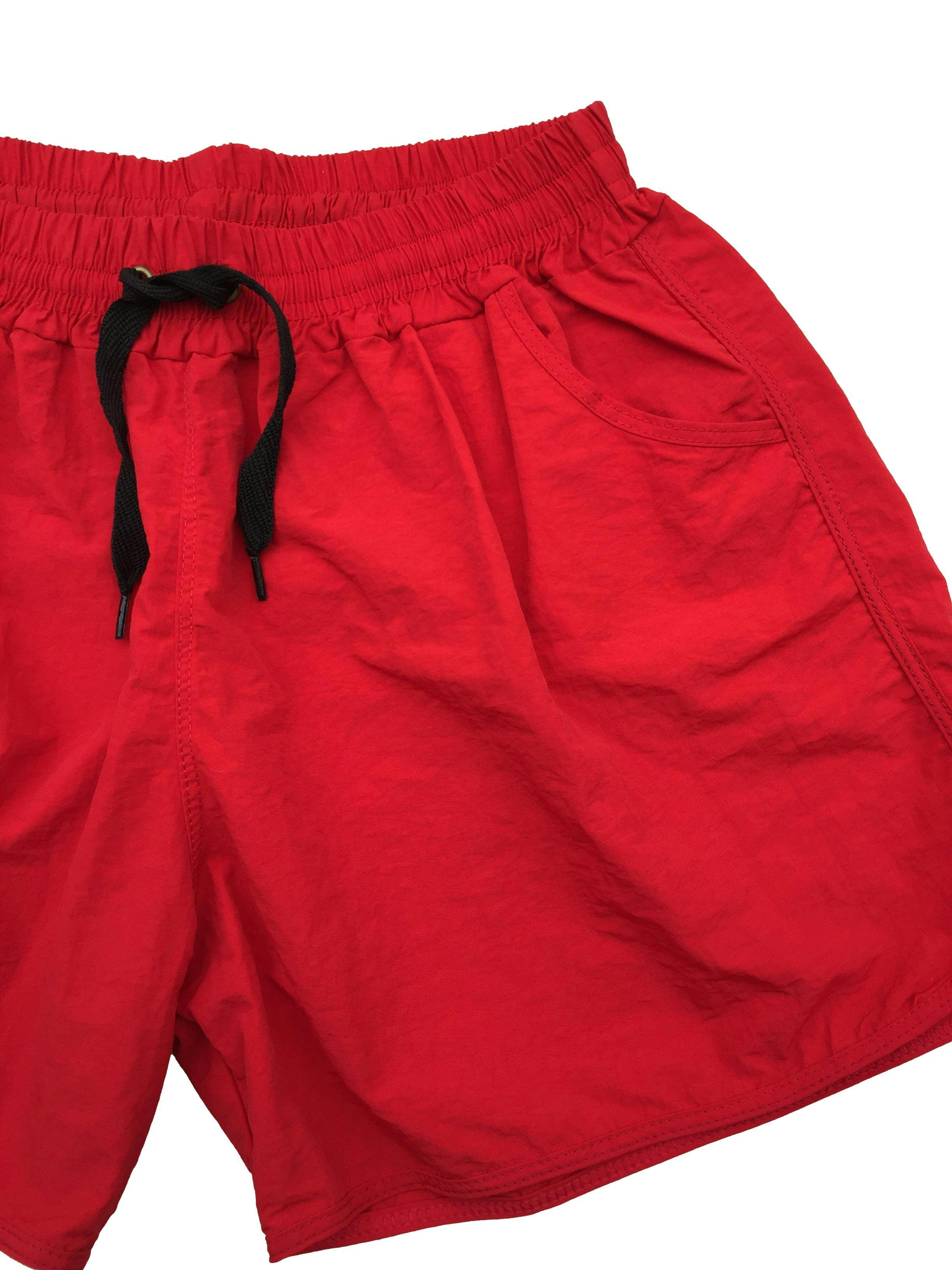 Short rojo de tela impermeable, pretina elástica con cordones y bolsillos. Cintura 64cm sin estirar, Tiro 27cm Largo 33cm.